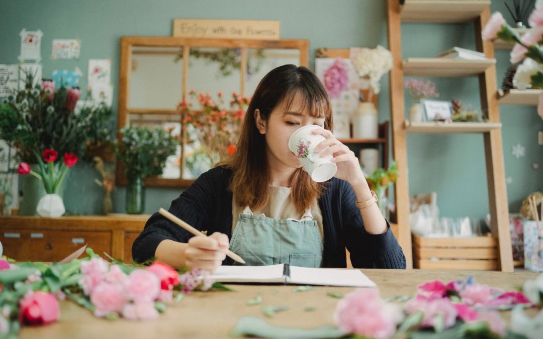 asian woman drinking coffee while working in floristry shop