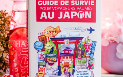 Le « Guide de survie pour voyageurs perdus au Japon » est posé sur une table rose, entouré de snacks japonais, avec en arrière-plan des décorations représentant des fleurs de cerisier.