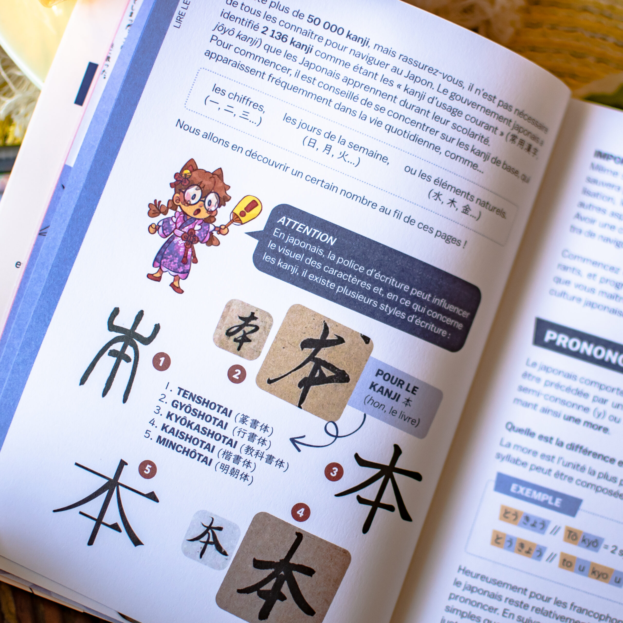 Une page extraite du *Guide de survie pour voyageurs paumés au Japon* présente le kanji japonais correspondant à « hon », avec des exemples manuscrits, des explications en français, une illustration du caractère et des schémas indiquant l'ordre des traits pour vous aider à vous entraîner à écrire ce kanji.