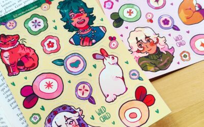 Les autocollants « Two Wild Child - Planches » au format A6, représentant des personnages de dessins animés, des animaux et des fleurs dans des motifs jaunes et roses, sont posés sur une surface en bois. Un livre ouvert apparaît dans le coin inférieur gauche.