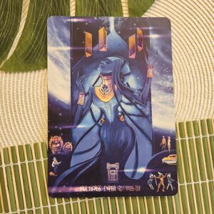 Une carte stylisée représente un personnage majestueux et futuriste, vêtu de bleu et paré de bijoux dorés, sur un fond cosmique parsemé de symboles et de formes holographiques. Le personnage lève les yeux vers le ciel, les mains levées, entouré de détails complexes et lumineux.