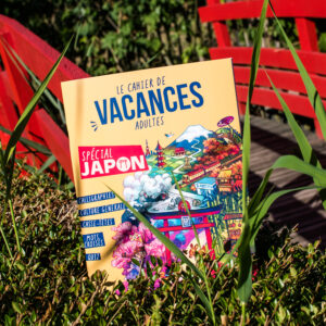 Un livre d'activités en français intitulé « Guide de survie pour voyageur paumé au Japon » repose dans des buissons verts près d'un pont en bois rouge ; sa couverture colorée est ornée d'illustrations représentant des sites emblématiques japonais.