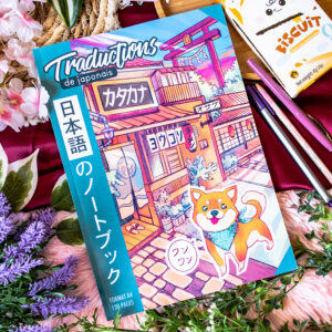 Le cahier « Traductions de Japonais 日本語のノートブック » (Shiba inu 柴犬) – format A4 présente une couverture aux couleurs vives ornée d'un chien Shiba Inu dessiné dans un style bande dessinée, d'un bâtiment traditionnel en bois et d'un texte en japonais, le tout entouré de fleurs, de stylos et d'un paquet de biscuits.