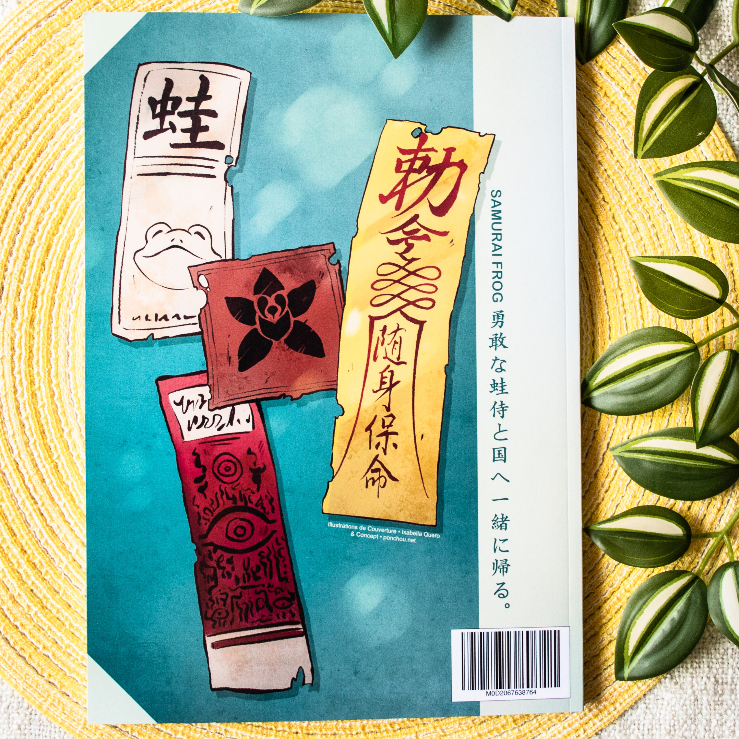 Quatre talismans en papier illustrés, comportant du texte en japonais, sont représentés sur un fond turquoise, avec un code-barres de livre et une plante feuillue sur le côté. La légende « SAMURAI FROG » et une inscription en japonais sont visibles à droite.